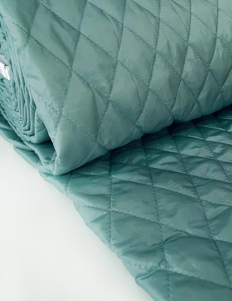 May include: A roll of teal quilted fabric with a diamond pattern. The fabric is folded in half and the edges are visible.