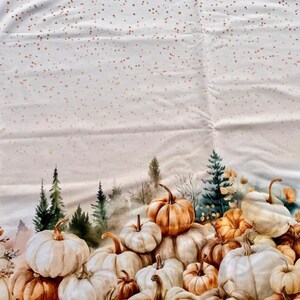 Könnte beinhalten: Stoff mit Herbstthema mit einem Haufen Kürbissen in Weiß-, Orange- und Brauntönen. Die Kürbisse befinden sich vor einer Waldszene mit immergrünen Bäumen. Die Oberseite des Stoffes hat ein Muster aus kleinen, goldfarbenen Punkten.