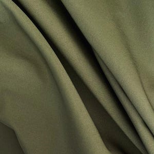 Könnte beinhalten: Nahaufnahme eines olivgrünen Stoffes mit weichen Falten und subtiler Textur. Der Stoff drapiert sich in sanften Wellen und erzeugt Schatten und Lichtreflexe. Die Farbe ist ein gedämpfter, erdiger Ton, der auf ein natürliches Material hindeutet.