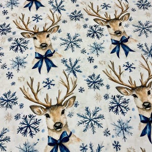 May include: White fabric featuring a repeating pattern of deer heads adorned with blue bows, alongside blue and white snowflakes. The deer have brown antlers and face forward. A winter holiday theme.
