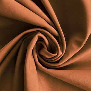 May include: A solid rust-colored fabric with a smooth, matte texture, arranged in a central spiral fold that creates deep, flowing shadows and highlights across the surface, emphasizing the drape and consistent color of the material.