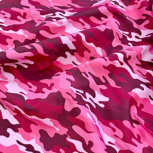 Pode incluir: Tecido de camuflagem rosa e branco com um padrão ondulado. O tecido é macio e tem uma textura lisa.
