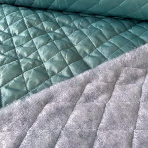 May include: A close-up of a teal quilted fabric with a grey quilted backing. The fabric is soft and has a diamond pattern.