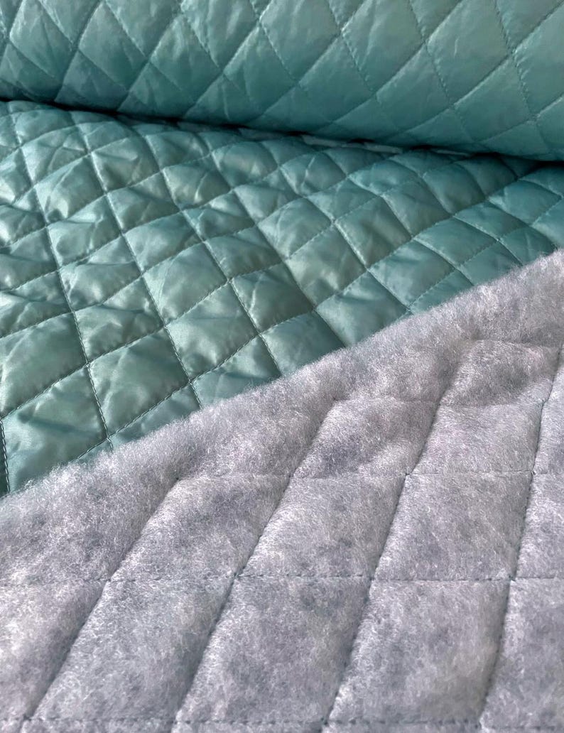 May include: A close-up of a teal quilted fabric with a grey quilted backing. The fabric is soft and has a diamond pattern.