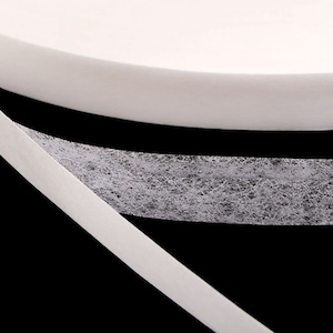 May include: White double-sided adhesive tape with a fuzzy texture on one side. The tape is rolled up and the fuzzy side is facing up.