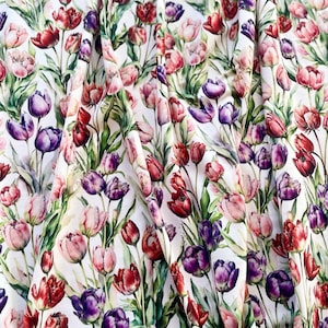 Pode incluir: Tecido branco com um padrão floral vibrante de tulipas em tons de vermelho, roxo e rosa. As tulipas têm caules e folhas verdes, criando um design colorido e detalhado. O tecido é provavelmente para vestuário ou decoração de casa.
