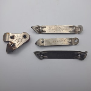 May include: A collection of vintage metal bottle openers. One is a folding style with "Quad Fold" printed on it. The others are flat, with text including "SHARP" and "SEL BEER". The openers are silver and show signs of wear.