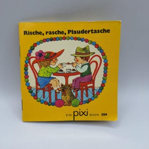 Peut inclure: Un livre pour enfants vintage avec une couverture jaune. L'illustration montre deux enfants à une table, un chien et le texte "Rische, rasche, Plaudertasche". Le livre est intitulé "Ein Pixi Buch 204".