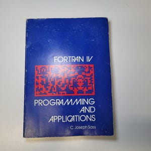 Op de afbeelding: Een vintage boek getiteld "FORTRAN IV PROGRAMMING AND APPLICATIONS" door C. Joseph Sass. De omslag is diepblauw met rode en witte tekst en een rode afbeelding. Het boek lijkt in goede staat te zijn.