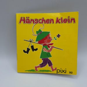 Peut inclure: Un livre pour enfants vintage avec une couverture jaune vif. Le titre "Hänschen klein" est en lettres rouges. L'illustration montre un garçon de dessin animé portant des bottes sur un bâton. Le livre est étiqueté "pixi 92".