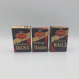 Puede incluir: Tres cajas vintage de suministros de ferretería de la marca Cross. Las cajas son negras con detalles en rojo y beige. Cada caja está etiquetada con el nombre del producto: TACKS, Staples y NAILS. El logotipo de Cross se muestra de forma destacada.
