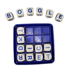 Op de afbeelding: Een Boggle-woordspelset met een blauw plastic rasterbord met zestien vierkante vakjes. Tien witte letterdobbelstenen liggen in het bord en zes extra dobbelstenen zijn in een boog erboven geplaatst, die samen het woord BOGGLE vormen.