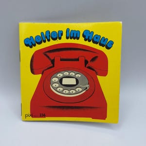 Peut inclure: Une couverture de livre pour enfants carrée et jaune avec une illustration de téléphone rotatif rouge. Le titre "Helfer im Haus" est en script bleu au-dessus du téléphone. Le livre est étiqueté "pixi" et "236" en bas à gauche.