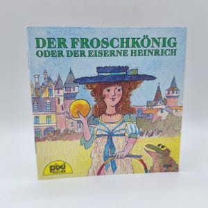 Peut inclure: Un livre pour enfants vintage intitulé "Der Froschkönig oder der Eiserne Heinrich" avec une illustration colorée. La couverture présente une femme tenant une balle dorée, une grenouille et un château en arrière-plan. Le livre est publié par Pixi Bücher.