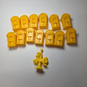 May include: A collection of thirteen small yellow plastic game pieces shaped like arched ticket booths and one yellow plastic game piece shaped like a carousel horse on a central pole, all arranged on a plain surface for board game play.