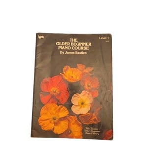 May include: A music instruction book titled The Older Beginner Piano Course by James Bastien, Level 1. The black cover features a vibrant illustration of orange and red poppy flowers across the bottom half, with white text detailing the title.