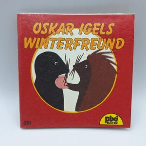 Peut inclure: Un livre pour enfants intitulé "Oskar Igels Winterfreund" avec une couverture rouge. La couverture présente une illustration circulaire d'une taupe et d'un hérisson. Le livre porte le numéro "521" et le logo "pixi BUCHER".