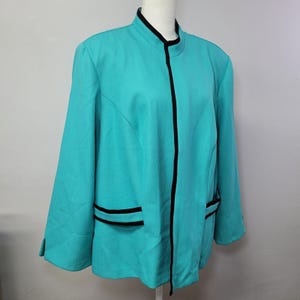 May include: A bright turquoise jacket featuring a mandarin collar and a vertical black trim running down the center front. The jacket includes long sleeves with small slits at the cuffs and two horizontal pockets, each accented with a black trim.