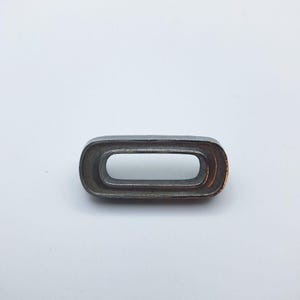 May include: A single, metallic gray eyelet with a rectangular shape and rounded corners. The eyelet has a smooth, slightly reflective surface and a hollow center. It is set against a plain white background.