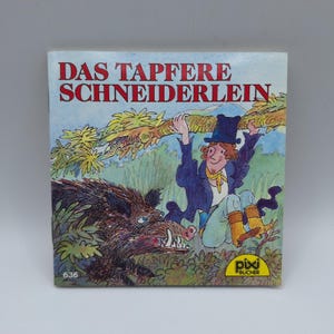 Peut inclure: Couverture de livre pour enfants avec le titre "DAS TAPFERE SCHNEIDERLEIN" en rouge. L'illustration représente un homme en manteau bleu et chapeau haut de forme suspendu à une branche d'arbre, avec un sanglier en dessous. Le livre a un logo "pixi BÜCHER".