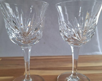 May include: Two clear crystal wine glasses with a cut glass design. The glasses have a tall stem and a round base.