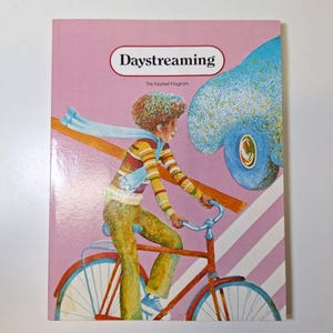 May include: A book cover with the title "Daystreaming" in a white oval on a pink background. The illustration depicts a person riding a red bicycle, with a blue car in the background.