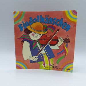 Peut inclure: Couverture de livre pour enfants vintage avec le titre "Fiedelhänschen" en script bleu. L'illustration représente un personnage de dessin animé jouant du violon, portant un chapeau et des vêtements colorés. Le fond est saumon avec des accents arc-en-ciel.
