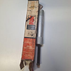 May include: An original Tecumseh Engines service part. The image shows a metal tool with a threaded rod and a box with the Tecumseh Engines logo and text. The box is worn and has the text "Original Service Part".