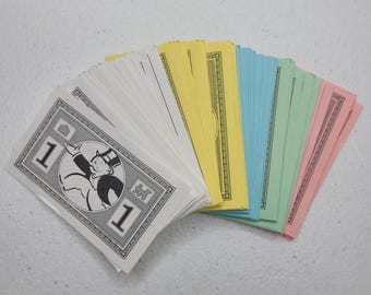 May include: A collection of Monopoly money, fanned out to display the different colors. The bills are white, yellow, blue, green, and pink. The white bills feature a black and white illustration of a man in a top hat.