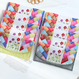 Pode incluir: Bolsas de tecido patchwork feitas à mão com padrões geométricos coloridos e desenhos florais bordados. As bolsas apresentam uma variedade de cores, incluindo vermelho, azul, verde e amarelo. As bolsas estão empilhadas.