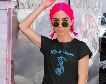 Puede incluir: Una camiseta negra con un gráfico de sirena y el texto "Hija de Yemaya" en letras azules.