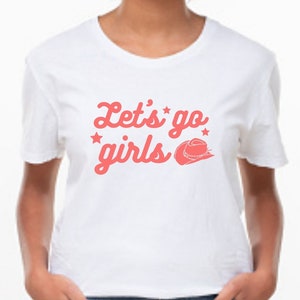 May include: White t-shirt with a pink graphic that says "Let's go girls" with a pink cowboy hat graphic.