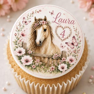Könnte beinhalten: Ein runder Cupcake-Aufleger mit einem hellbraunen Pferd mit Blumenkranz, das hinter einem Holzzaun steht. Das Design zeigt rosa Blumen, Schmetterlinge, einen herzförmigen Rahmen mit der Zahl 4 und den Namen Laura in rosa Schreibschrift.