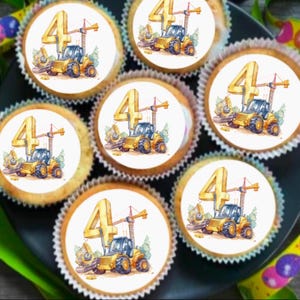 Könnte beinhalten: Sechs gelbe und weiße Cupcakes, verziert mit essbaren Bildern eines gelben Baufahrzeugs mit einem Kran und der Zahl vier. Die Cupcakes sind auf einem schwarzen Teller angeordnet.
