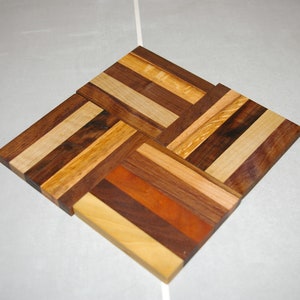 May include: A square wooden coaster made of different types of wood, including walnut, maple, and cherry. The wood is arranged in a geometric pattern, creating a unique and stylish design.