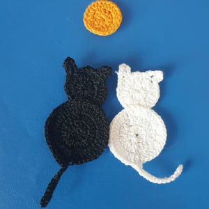 May include: Crocheted cat and moon applique set. The set includes a black cat, a white cat, and a yellow moon. The cat appliques are round with pointed ears and a tail. The moon is a small, round shape. The background is blue.