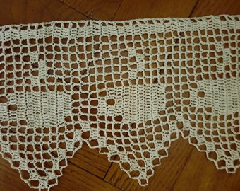 May include: A close-up of a white crocheted lace trim with a scalloped edge. The lace is made with a delicate pattern of squares and circles.