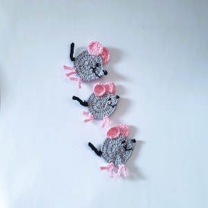 May include: Three handmade crochet mice in a row. Each mouse has a gray body, pink ears, black eyes and whiskers, and pink feet. The mice are displayed on a white background.