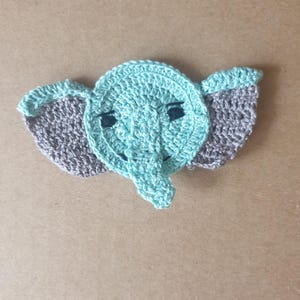 Può includere: Un elefante all'uncinetto con orecchie grigie e un corpo blu chiaro. L'elefante ha occhi neri e una piccola proboscide.
