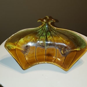 May include: A brown and green ceramic dish with a unique, fan-shaped design. The dish has a glossy finish and a raised, decorative center.