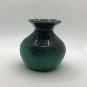 May include: A small, green and black ceramic vase with a rounded body and a flared lip.