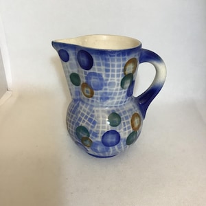 May include: A small, blue and white ceramic pitcher with a handle. The pitcher features a grid pattern with blue, green, and brown polka dots. The interior is white.