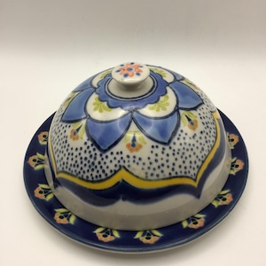 K&ouml;nnte beinhalten: Eine Keramik-Butterdose mit gew&ouml;lbtem Deckel und passendem Teller. Der Deckel hat ein blaues Blumenmuster mit gelben und orangefarbenen Akzenten. Teller und Deckel haben einen dunkelblauen Rand mit floralen Mustern.