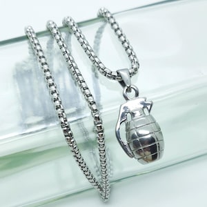 Op de afbeelding: Een zilverkleurige ketting met een granaat hanger. De hanger heeft een getextureerd oppervlak en een lus voor de ketting. De ketting heeft een schakelontwerp. De ketting wordt gepresenteerd op een helder oppervlak.