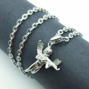 Pu&ograve; includere: Una collana a catena d'argento con un ciondolo a forma di cherubino che tiene una pistola. Il cherubino ha le ali ed &egrave; raffigurato in una posa di volo.