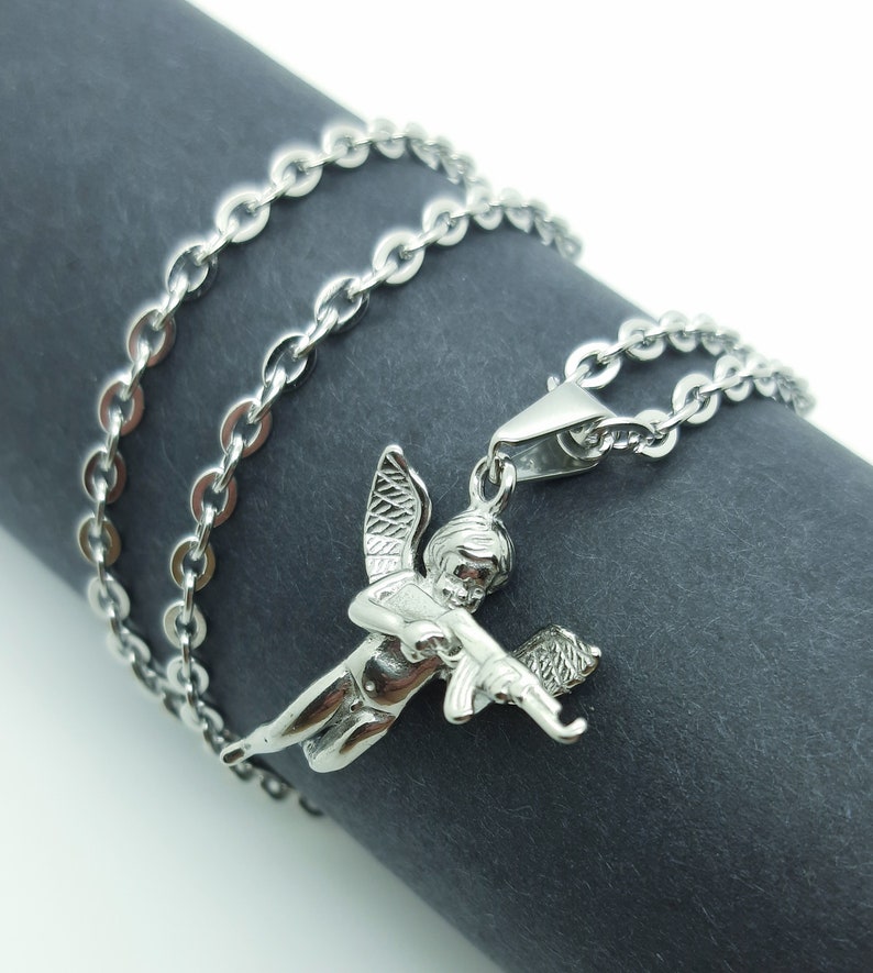 Pu&ograve; includere: Una collana a catena d'argento con un ciondolo a forma di cherubino che tiene una pistola. Il cherubino ha le ali ed &egrave; raffigurato in una posa di volo.