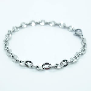 May include: A silver bracelet with a delicate chain design. The bracelet features small, flat, circular links connected to each other. The clasp is visible at the end of the bracelet. The jewellery is set against a white background.