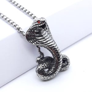 May include: A silver cobra pendant necklace with a red stone eye. The pendant is detailed with scales and the cobra is in a coiled position.