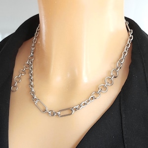 Peut inclure: Un collier chaîne argenté avec un mélange de maillons ronds et rectangulaires. Le collier est présenté sur un mannequin, sur fond noir.