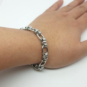 May include: A silver chain bracelet with a unique link design. The bracelet is made of metal and has a polished finish.